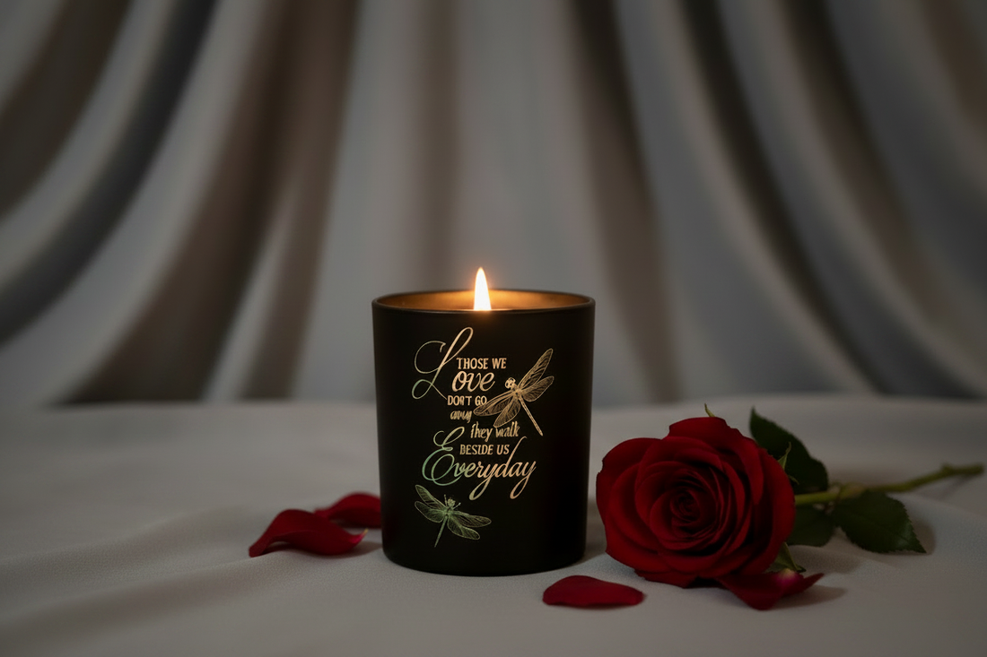A glowing black engraved Love candle with dragonfly design and a red rose on soft grey draped cloth