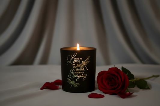 A glowing black engraved Love candle with dragonfly design and a red rose on soft grey draped cloth